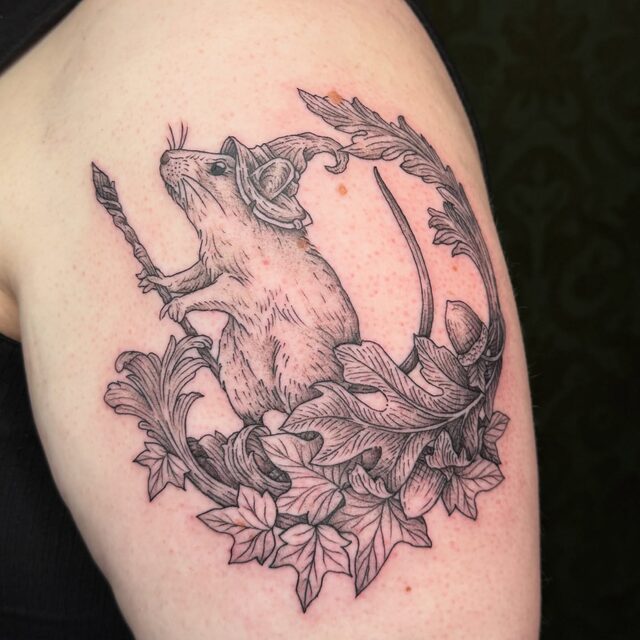Rat with a sword inside a crescent of leaves, tattooed on an upper arm