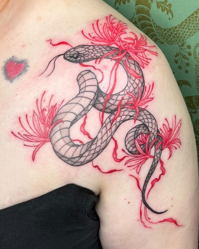 Black and grey serpent coiled through red spider lilies, tattooed on a shoulder