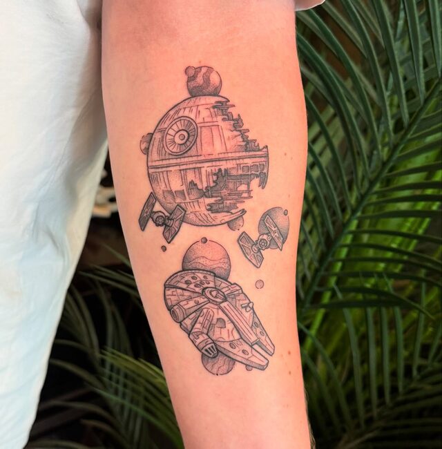 The Death Star and the Millennium Falcon in black and grey, tattooed on a forearm