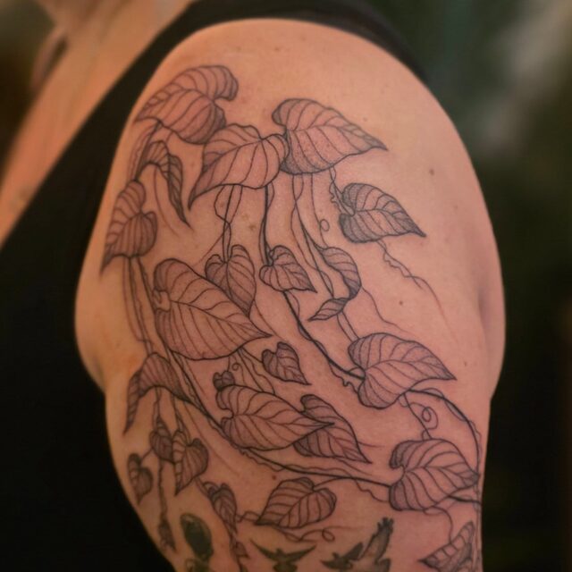 Fine-line tattoo of trailing heart-shaped ivy leaves over a shoulder