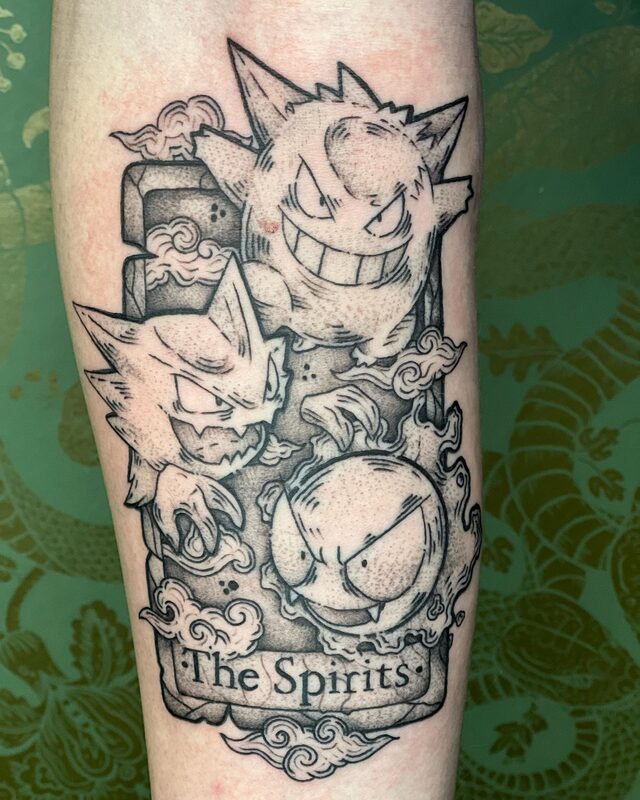 Tarot card tattoo titled The Spirits with Gengar, Haunter and Gastly among clouds, on a forearm