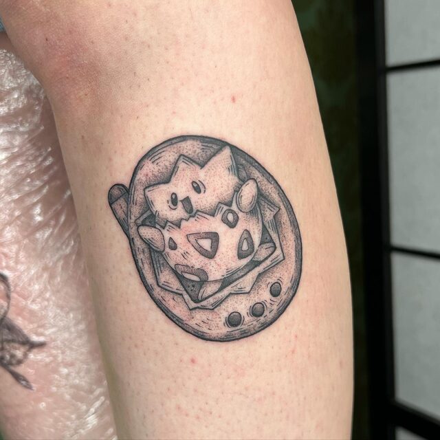 Stippled tattoo of the Pokémon Togepi inside an oval Tamagotchi with three buttons