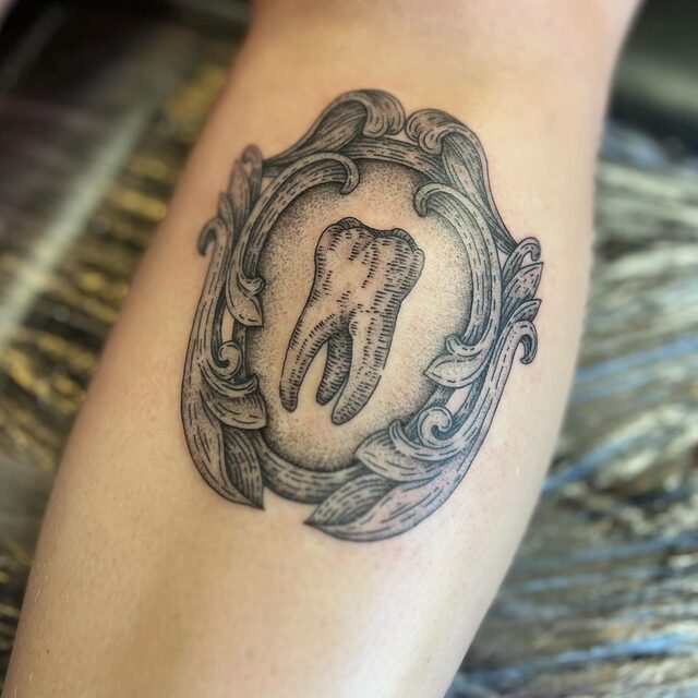 Etched tattoo of a tooth inside an ornate baroque picture frame, with a stippled background